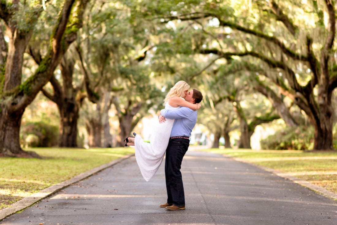 Man lifting fiance into the air under Live Oaks - Litchfield Plantation