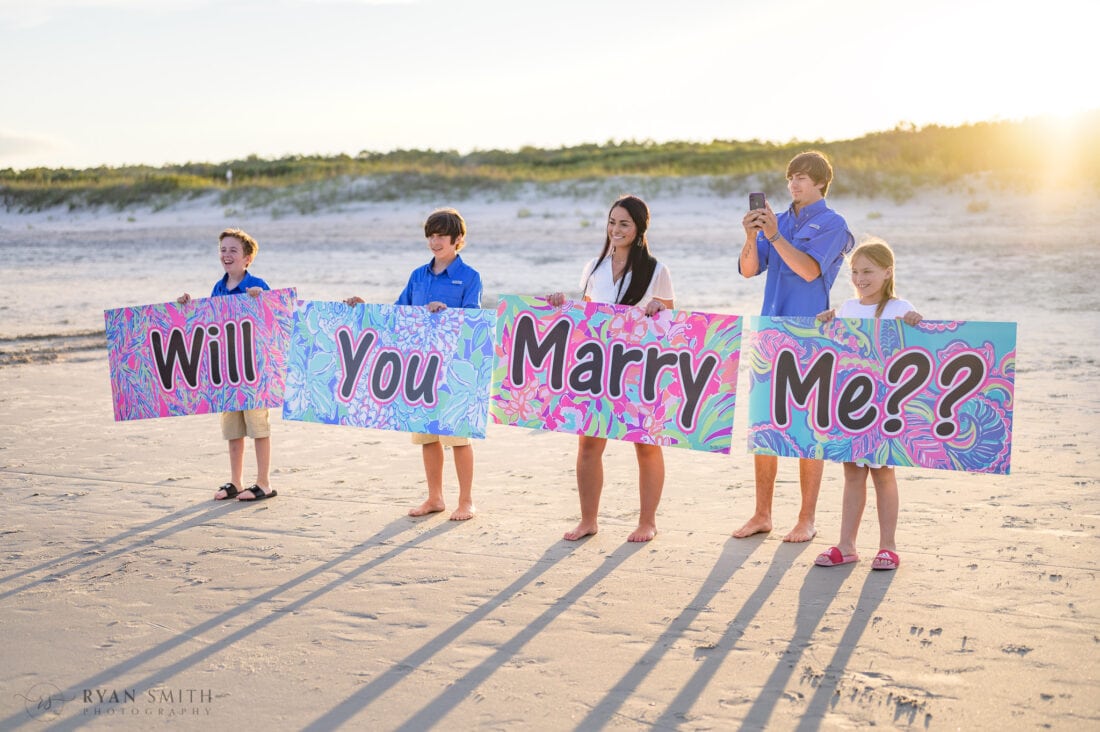 Kids holding up Will You Mary Me signs - Huntington Beach State Park