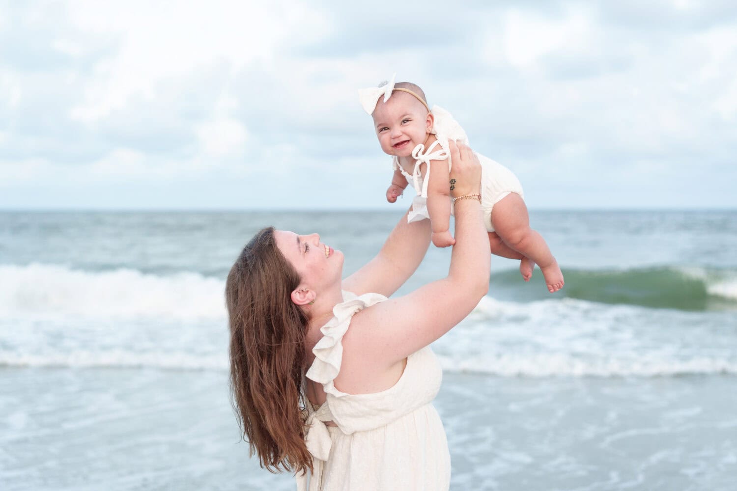 Mom holding happy baby in the air in front of the ocean - Huntington Beach State Park